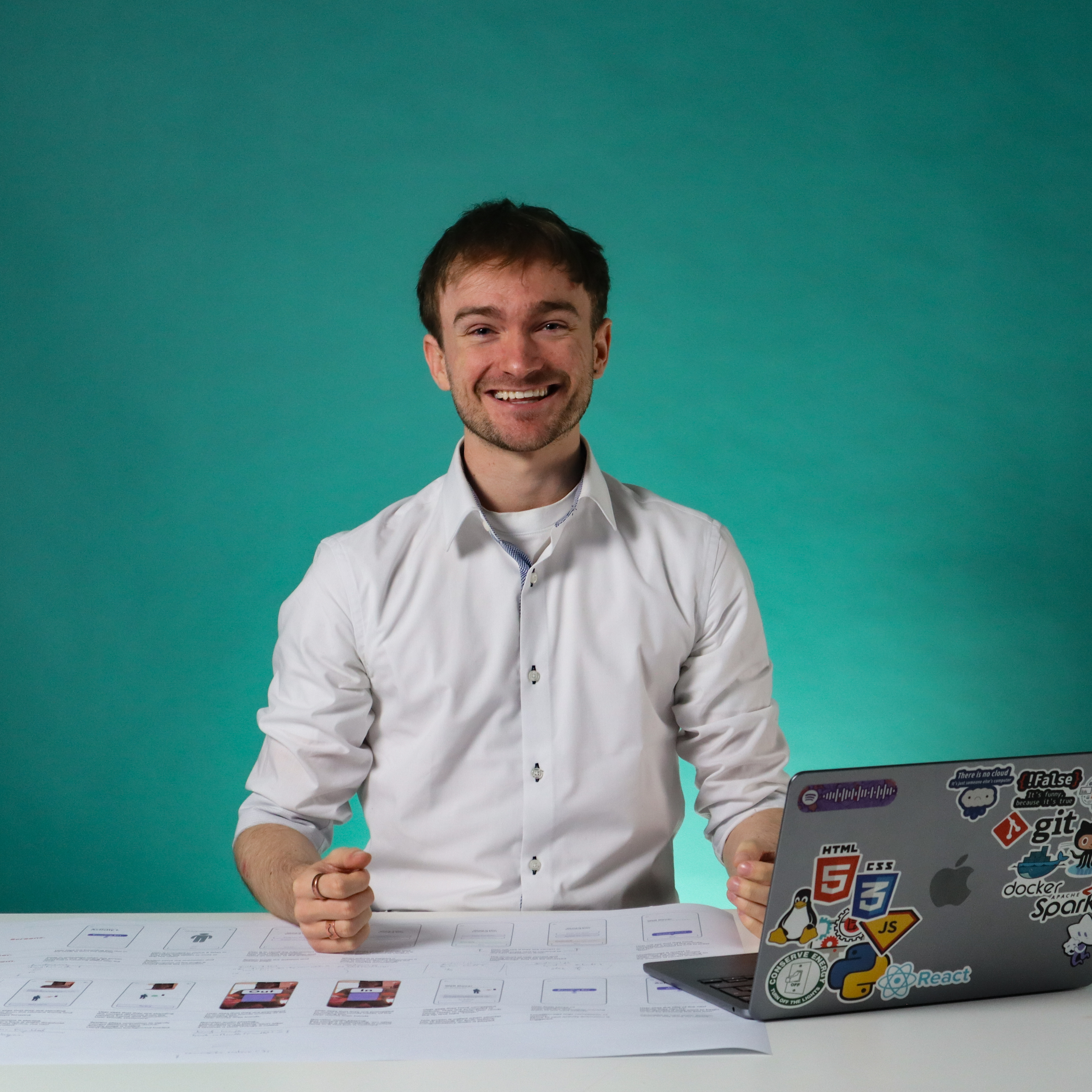 Thomas Kelly sitting at a desk smiling with a laptop and screen flows on the desk in front of him.